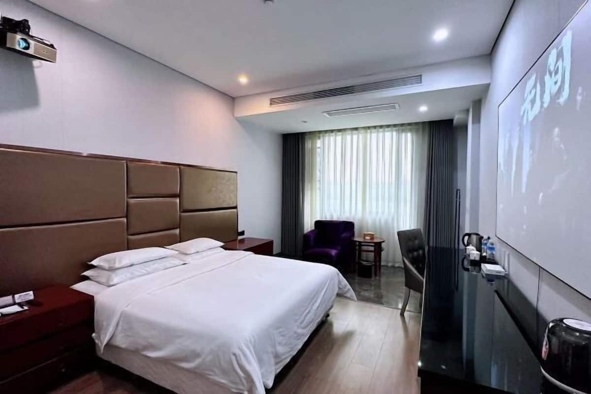 Habitación de hotel con una cama grande, un escritorio con silla, una pantalla de proyector y vistas al exterior a través de la ventana.