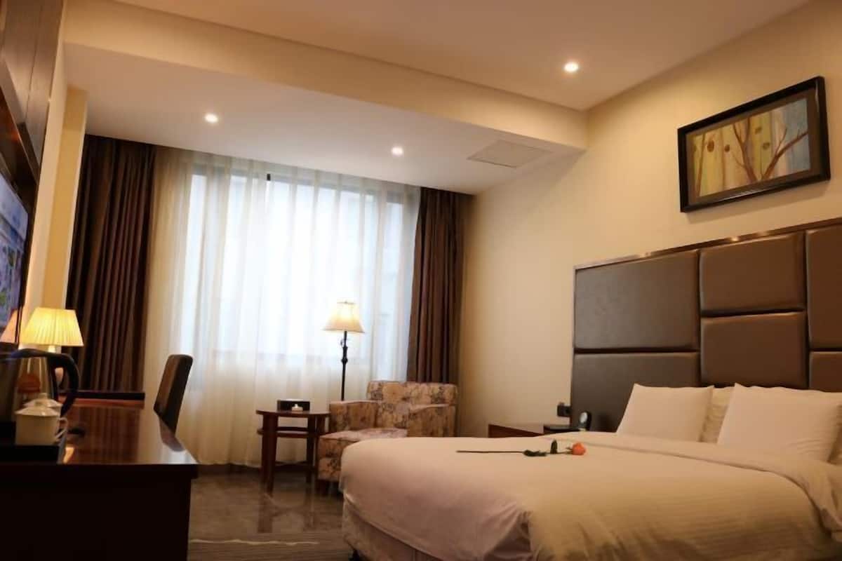 Una habitación de hotel con cama, escritorio, silla, lámpara y un cuadro en la pared.