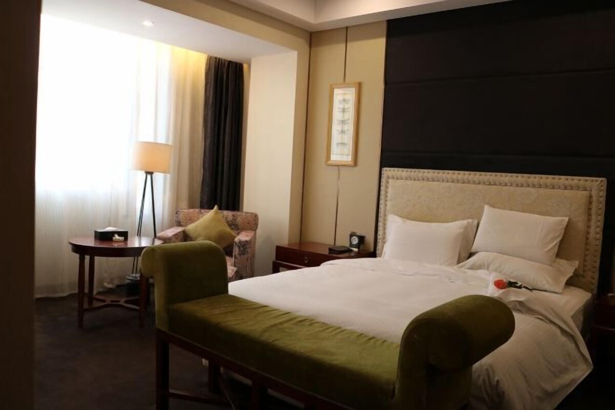 Une chambre d’hôtel avec un grand lit, une table de chevet, une chaise, une lampe et un tableau encadré au mur.