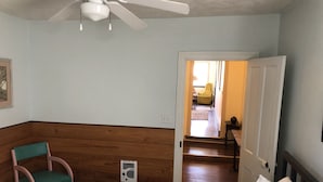 A bedroom with a bed, a chair, a ceiling fan, and a door leading to another room.
