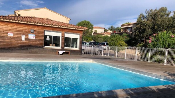A swimming pool with a wooden deck, a building with a tiled roof, and a white fence. - Apartment in residence with swimming pool, janitor, 7 minutes walk from the beach (Zonza)