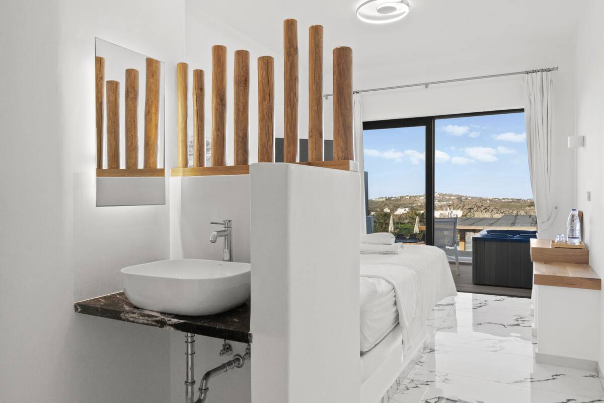 A modern bathroom with a large sink, a mirror, wooden vertical elements, and a view of the outdoors.