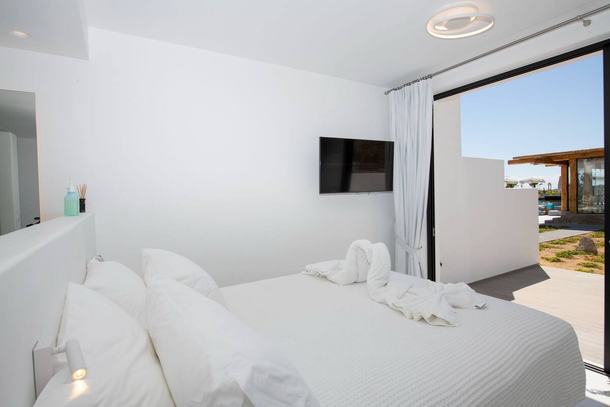A modern hotel room with a large bed, a flat-screen TV, and a sliding glass door leading to an outdoor area.