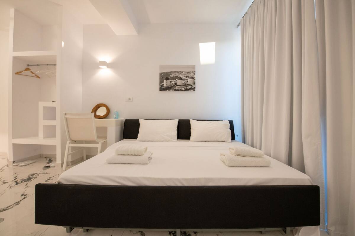 A neatly arranged bedroom with a bed, a chair, a desk, and a hanging coat rack.