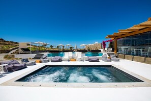 Un área de piscina en la azotea con sillones, sombrillas y un jacuzzi.