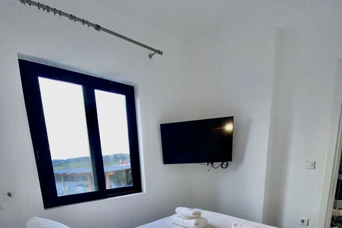 A bedroom with a large bed, a TV mounted on the wall, and a window providing a view of the outdoors.