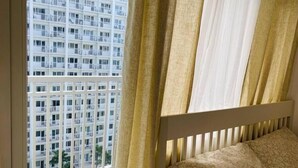 A bedroom with a view of a high-rise building through a window with curtains. - Relax in Style: Your Private Paradise Awaits at Dtravellers Home at Shore MOA (Pasay)