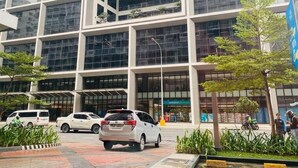 A modern building with multiple floors, large windows, and a parking area with cars. - Relax in Style: Your Private Paradise Awaits at Dtravellers Home at Shore MOA (Pasay)