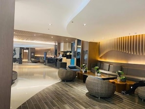 A modern hotel lobby with a reception desk, seating area, and a curved wall with vertical panels.