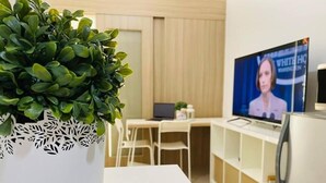 A modern room with a white desk, a laptop, a flat-screen TV, and a potted plant. - Relax in Style: Your Private Paradise Awaits at Dtravellers Home at Shore MOA (Pasay)