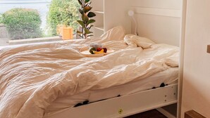 A bed with a wooden frame, a bedside table with a plant, and a window with a view of a lake and hills.