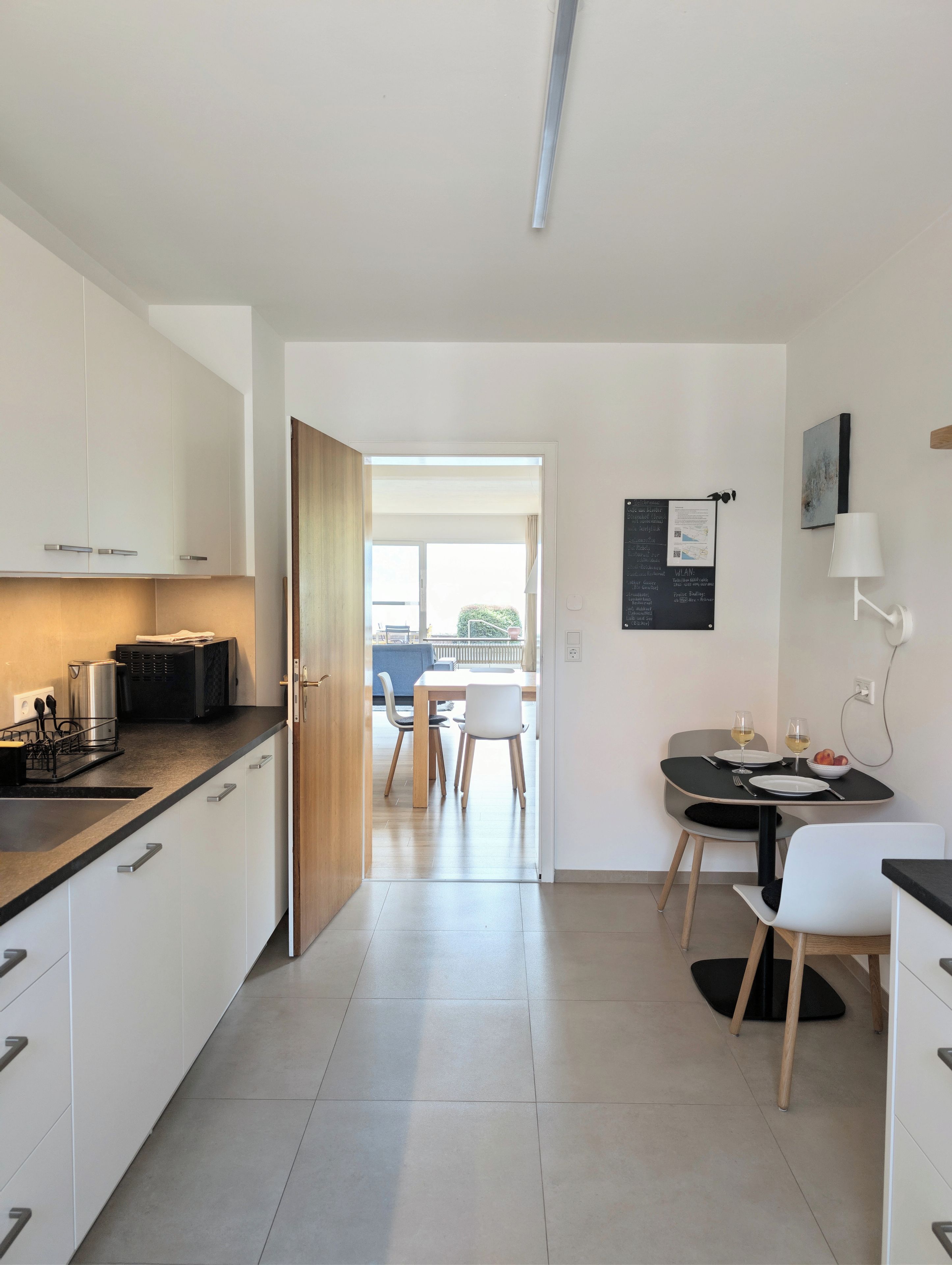 A modern kitchen with white cabinets, a dining area with a table and chairs, and a view to an outdoor balcony.