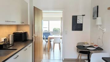 A modern kitchen with white cabinets, a dining area with a table and chairs, and a view to an outdoor balcony.