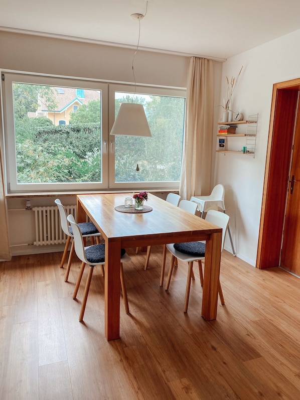 Un coin repas avec une table en bois, quatre chaises, une lampe suspendue et une vue sur la verdure à l’extérieur.
