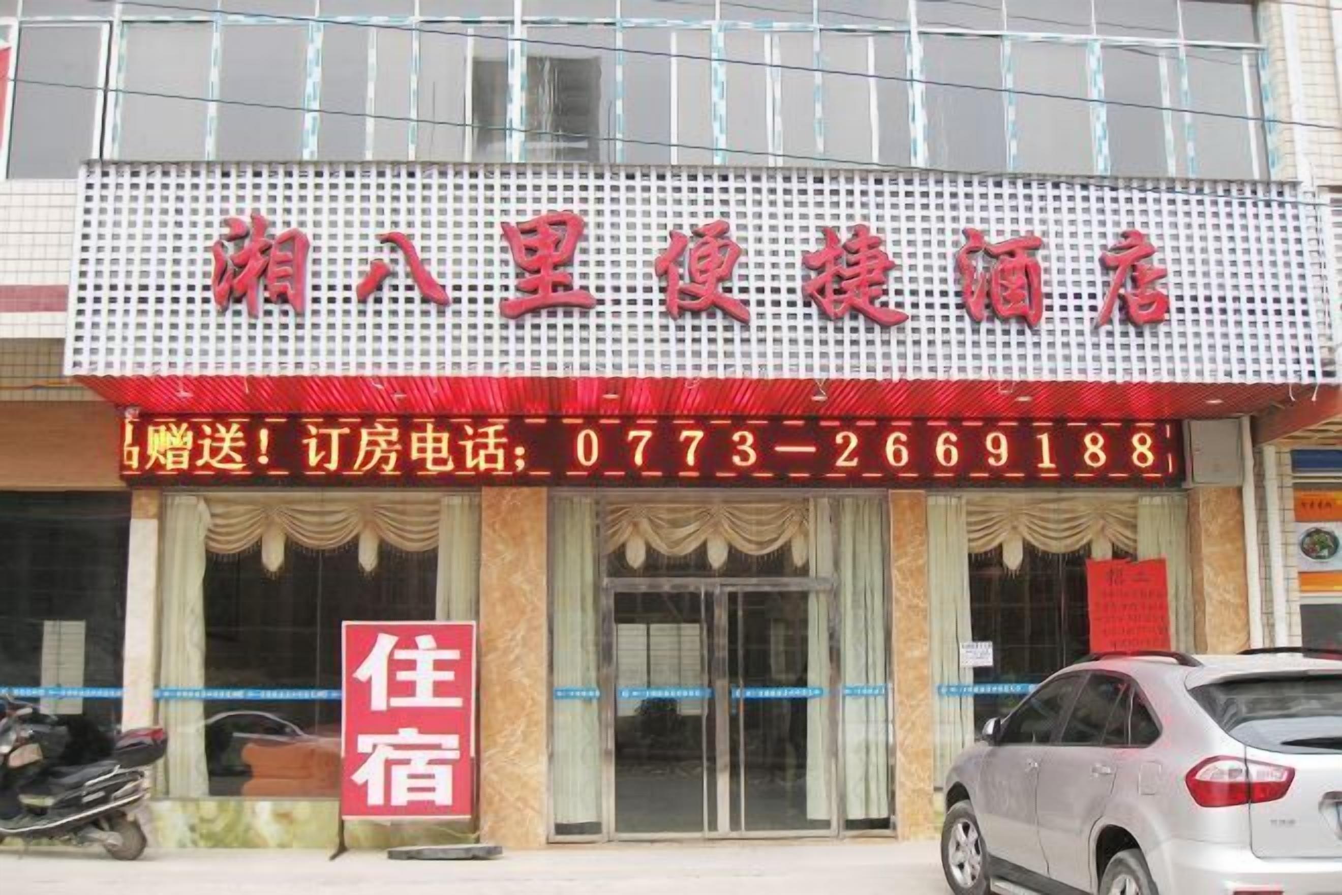 A hotel with a prominent red signboard displaying the name and contact number.