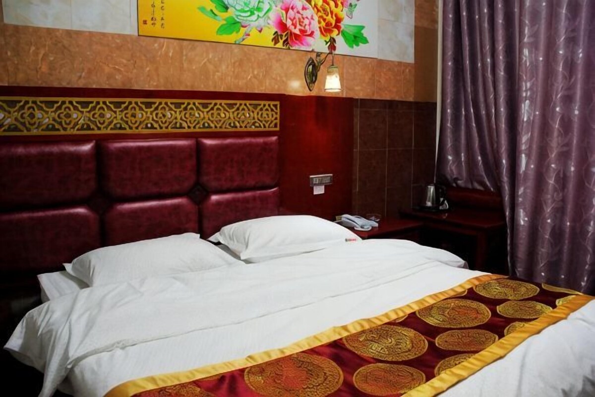 A hotel room with a large bed, a headboard with a geometric pattern, a bedside table with a phone, and a curtain.