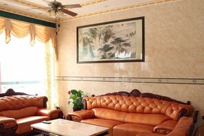 A room with a leather sofa, a ceiling fan, a framed artwork, and a window with curtains. - Xiangbali Express Hotel Guilin (Lingchuan)