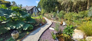 Stroll through the lush garden, surrounded by a variety of plants and a serene pond, to the charming house with a pitched roof.