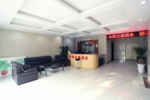 Un hall dâhĂŽtel comprenant un comptoir dâaccueil, un espace salon et une plante en pot.