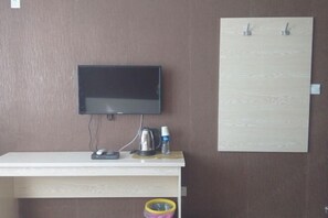 Una habitación con una televisión de pantalla plana montada en la pared, un escritorio blanco con una tetera, una botella de agua y un ratón.