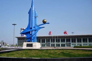 Una escultura azul abstracta, un edificio con fachada de vidrio y un cielo despejado.