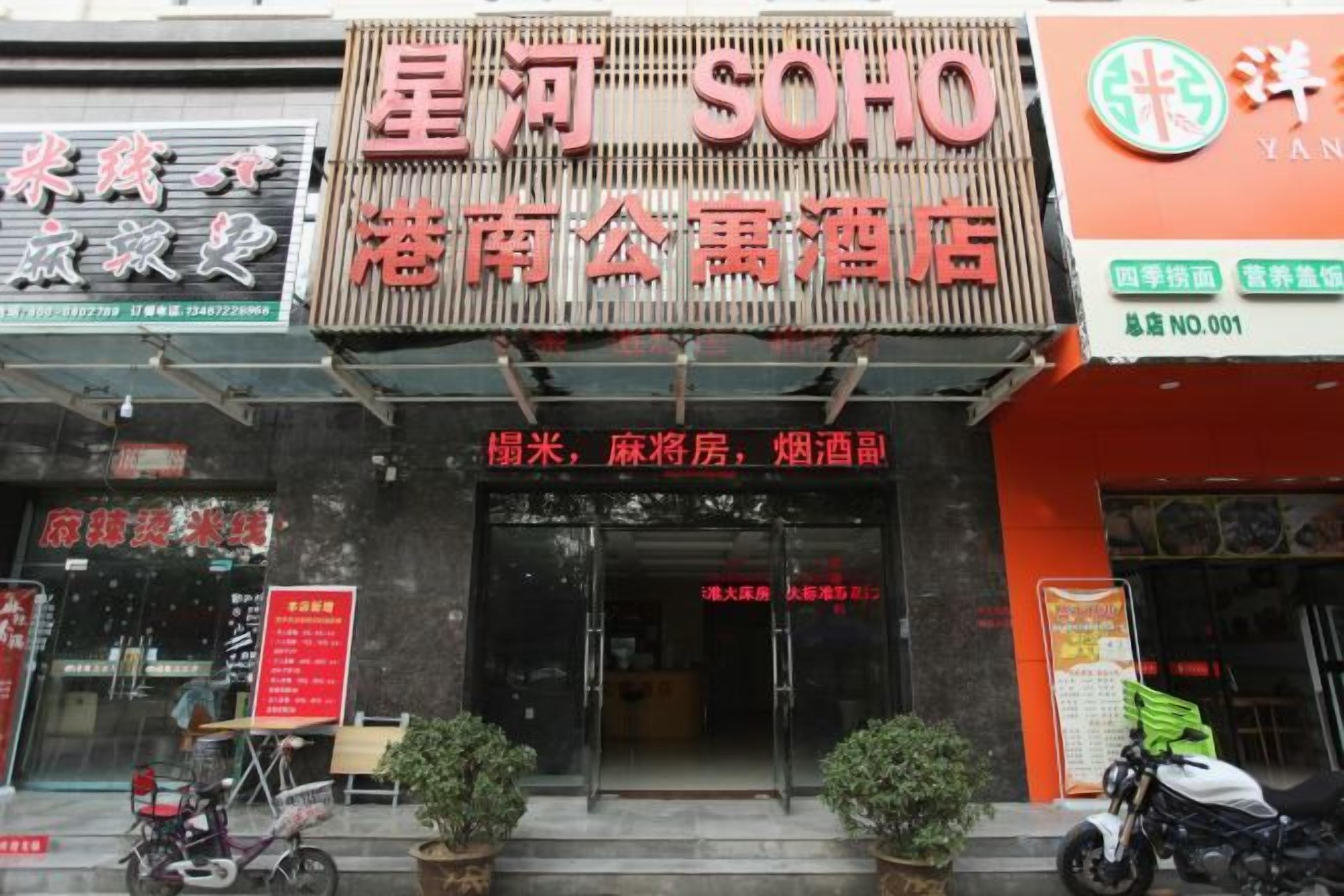A hotel entrance with a prominent sign, a bicycle parked outside, and a motorcycle to the right.