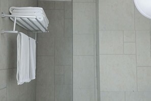 Une salle de bain avec un porte-serviettes où sont pliées les serviettes, un espace douche et un sol carrelé.