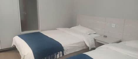 A hotel room with two beds, a nightstand, a window, and a door.