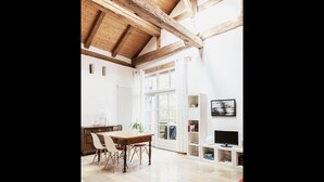 Una habitación amplia con techo de madera, una mesa de comedor con sillas, un sofá rojo y un televisor sobre un soporte blanco.