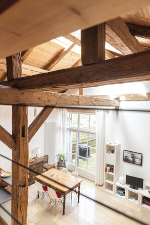 A room with a wooden ceiling, a dining table with chairs, a television, and a window with curtains.