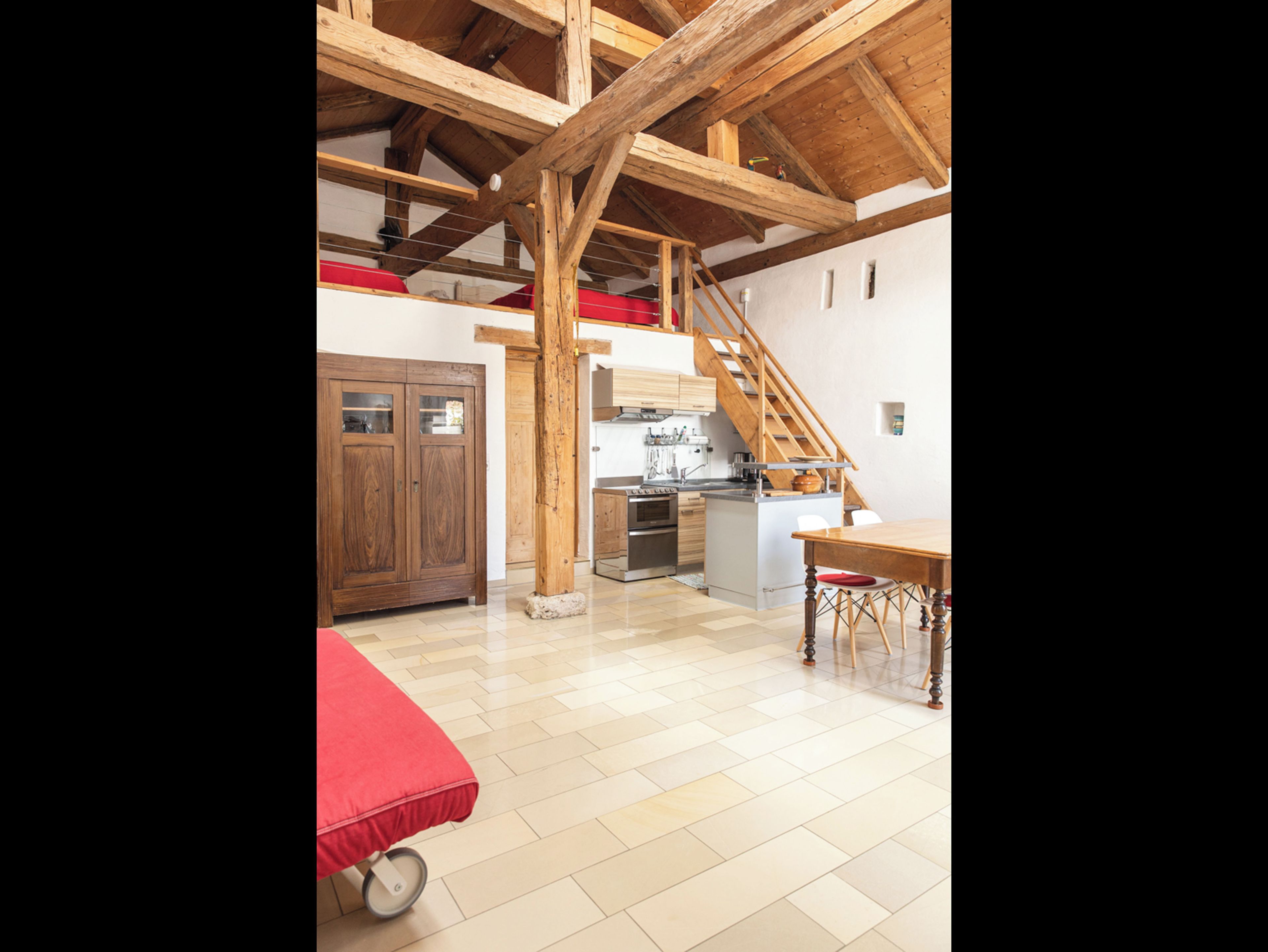 A spacious loft with a high ceiling, wooden beams, a kitchen area, and a dining table.