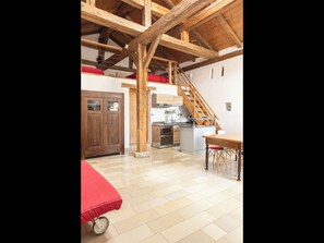 A spacious loft with a high ceiling, wooden beams, a kitchen area, and a dining table.