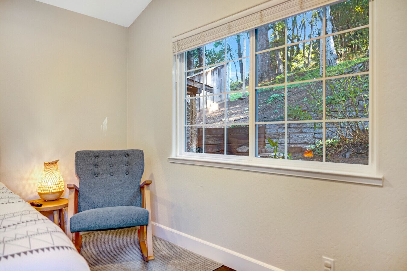 A bedroom with a large window, a chair, a lamp, and a bed.