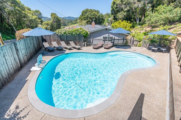 A swimming pool with lounge chairs and umbrellas, surrounded by a wooden fence and a house in the background. - Private Pool Villa for family getaways (Aptos)