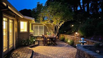 A patio with a brick floor, a wooden table with chairs, and a small garden area with a fountain.