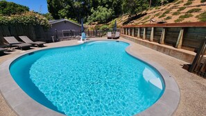 A swimming pool with a curved edge, surrounded by a concrete deck and a wooden fence. - Private Pool Villa for family getaways (Aptos)