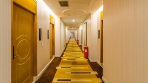 A hotel hallway with a carpeted floor, doors on both sides, and a red trash bin. - Weiyesi Hotel (Shenzhen)