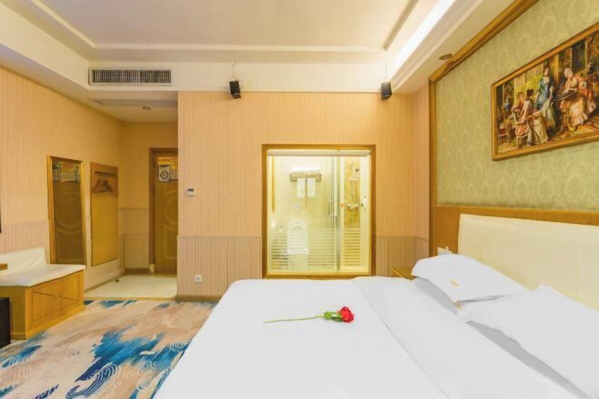A hotel room with a bed, a bathroom, a wardrobe, and a painting on the wall.