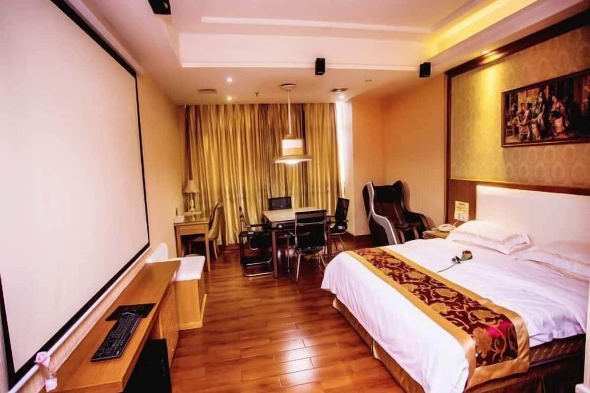 A hotel room with a bed, desk, chair, and a painting on the wall.