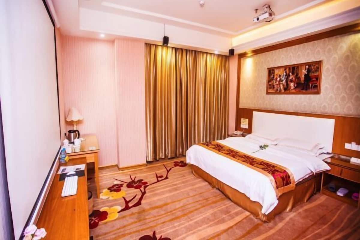 A hotel room with a bed, a desk with a lamp, a television, and a painting on the wall.