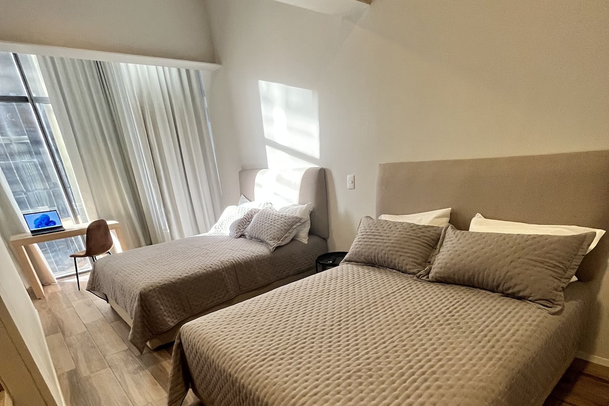 A modern hotel room with two beds, a desk, and a laptop.