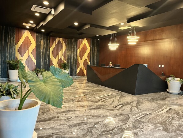 Un área de recepción moderna con piso de mármol, mostrador de madera y diseño de pared estampado.