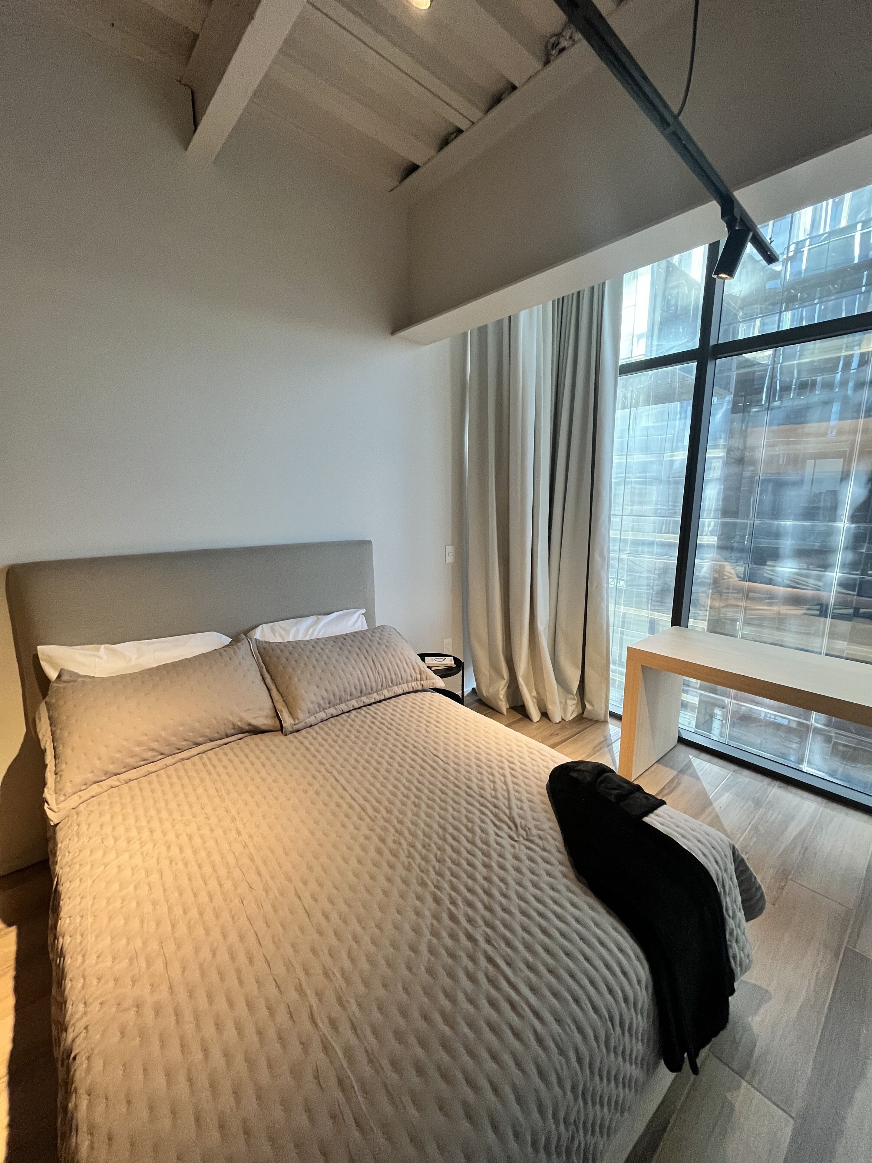 Un dormitorio moderno con una cama grande, un banco de madera y vistas de la ciudad a través de amplias ventanas.