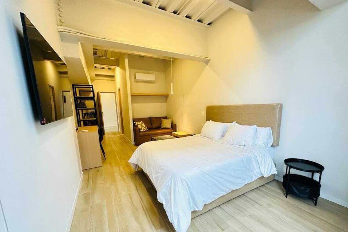 A bedroom with a bed, bedside tables, a TV mounted on the wall, and a small black table.