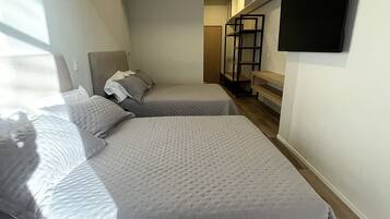 Un dormitorio con dos camas, un televisor instalado en la pared y una escalera que conduce a un nivel superior.