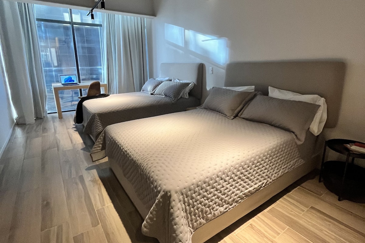 A modern hotel room with two beds, a desk, and a large window.