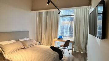 Une chambre d’hôtel moderne avec un grand lit, un bureau avec un ordinateur portable et un téléviseur fixé au mur.