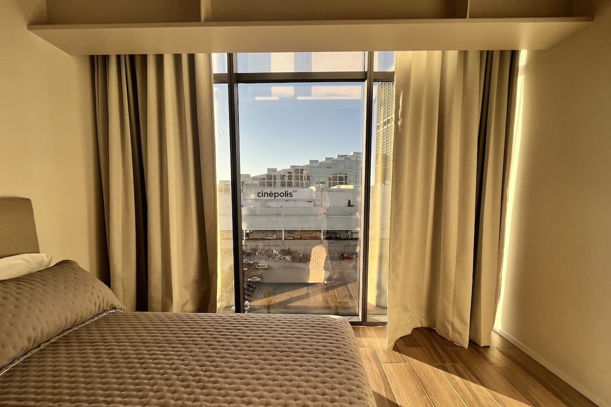 A hotel room with a bed, curtains, and a view of a building labeled 'cinépolis' through a glass door.