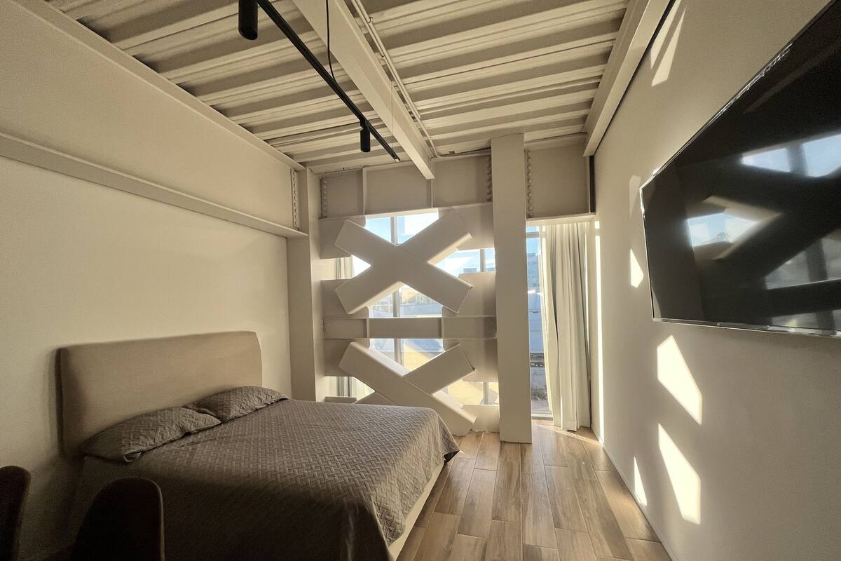 A modern bedroom with a bed, a TV, and a unique ceiling design.