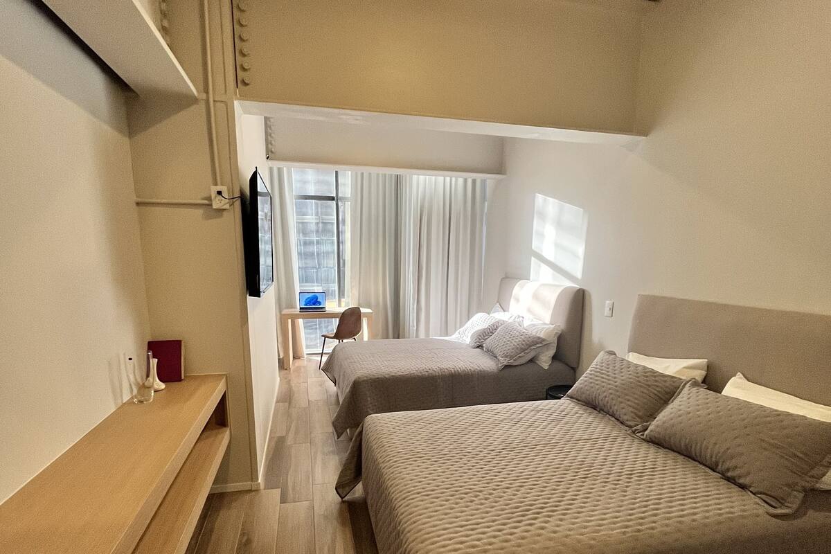 A hotel room with two beds, a desk, a TV, and a window with curtains.